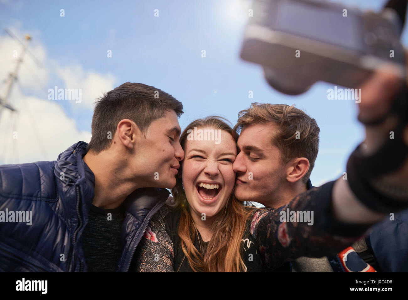 Tre amici prendendo selfie con fotocamera, giovani uomini kissing giovane donna sulla guancia, Bristol, Regno Unito Foto Stock