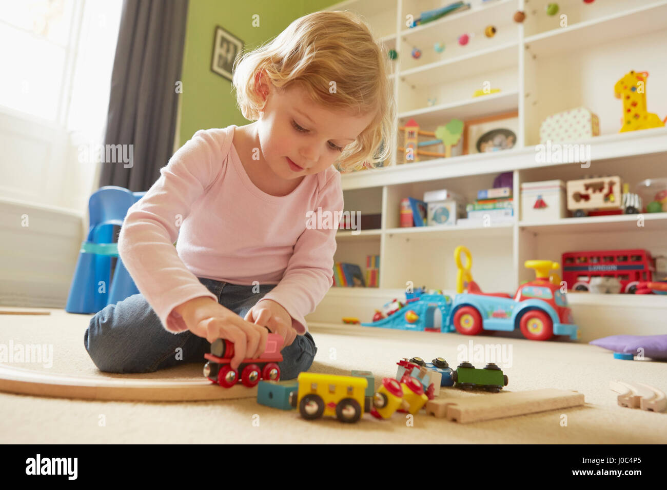 Toddler femmina giocando con il trenino sul pavimento nella sala giochi Foto Stock