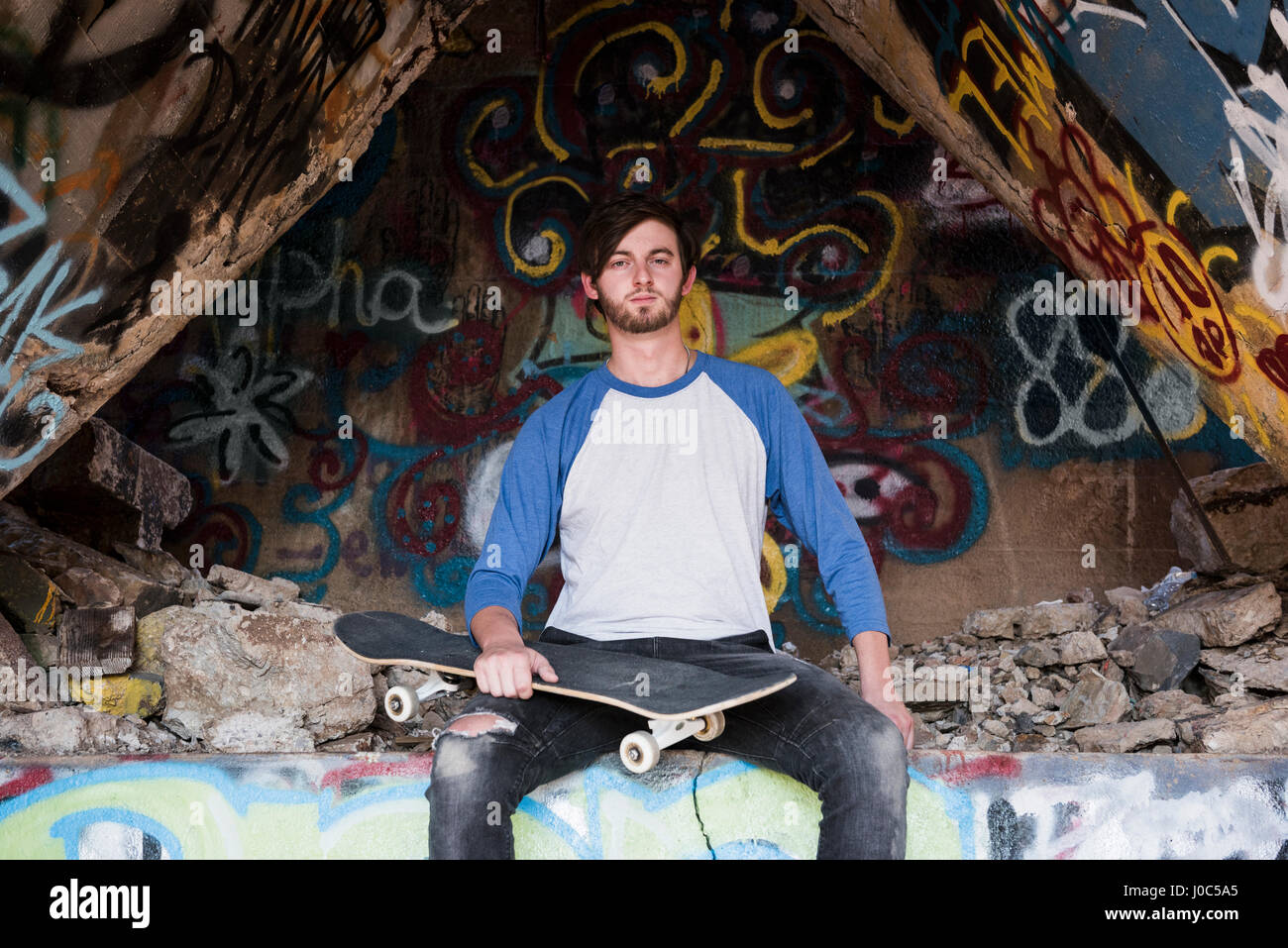 Ritratto di giovane maschio guidatore di skateboard seduto sul muro di graffiti a ha rovinato il mio Foto Stock
