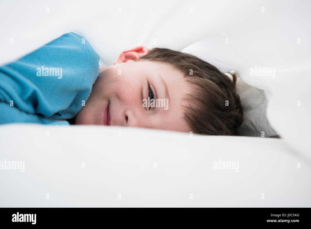 Ritratto di ragazzo che giace tra le bianche lenzuola Foto Stock