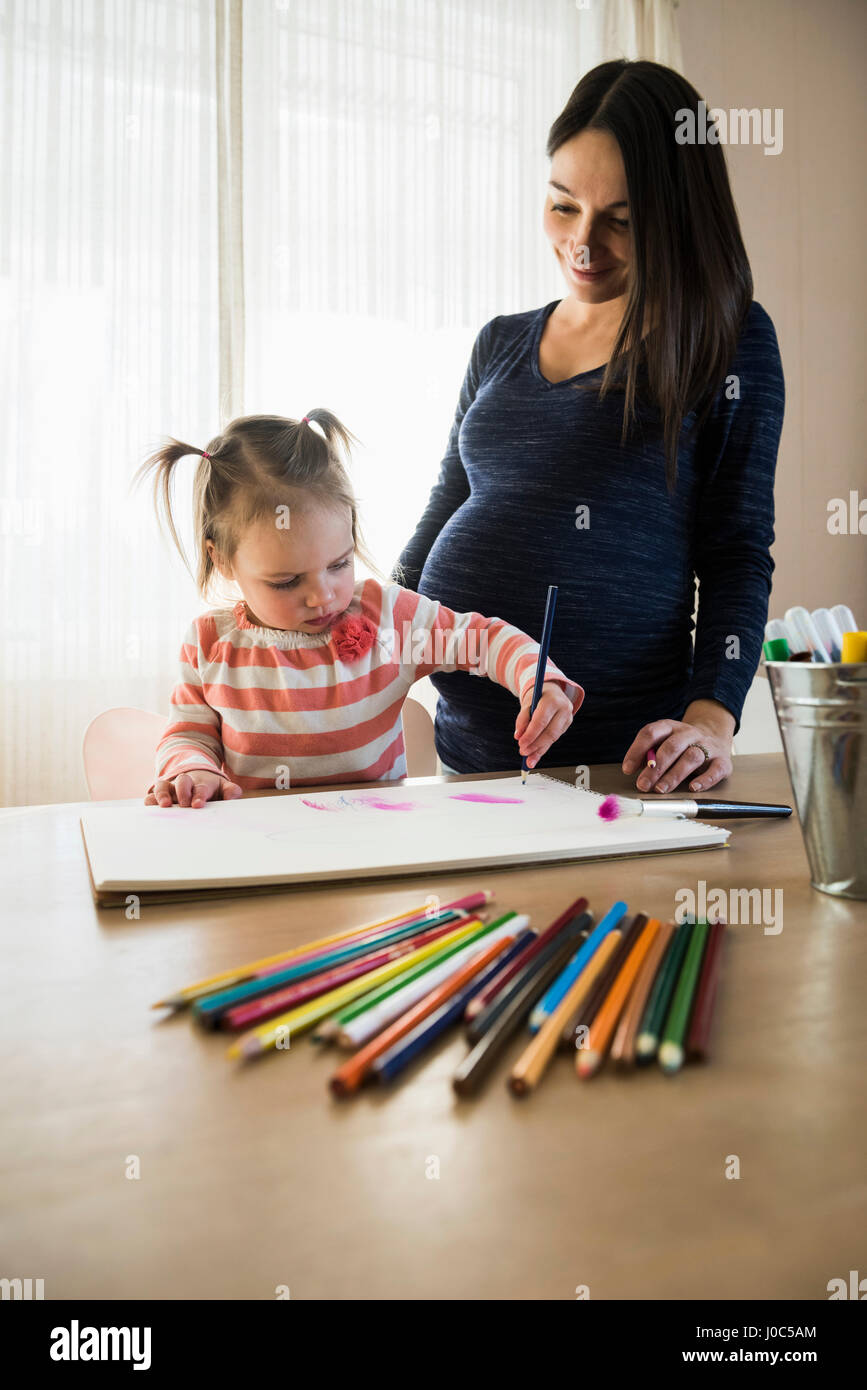 Toddler femmina a tavola con la gravidanza madre disegno in sketchbook Foto Stock