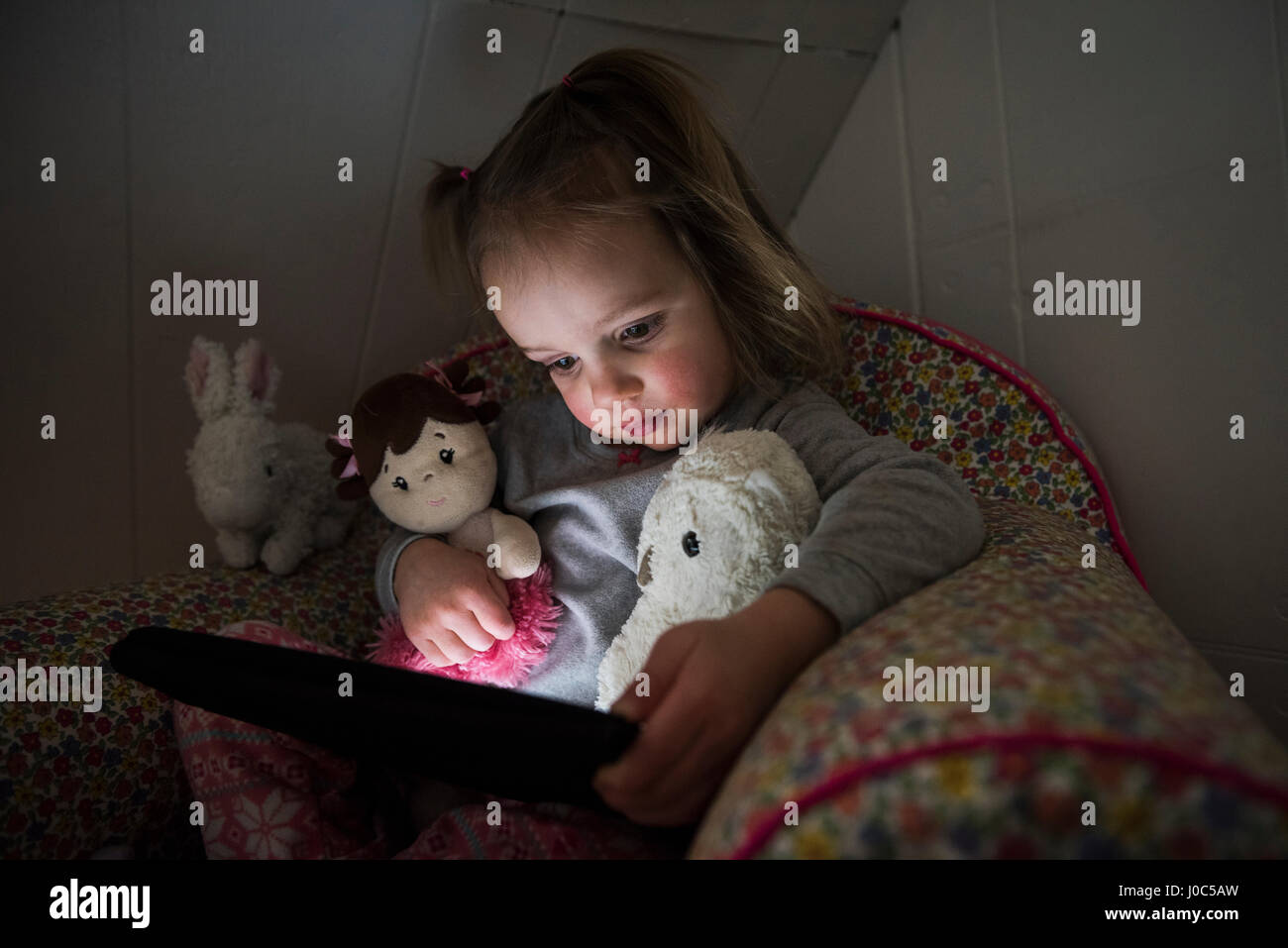 Toddler femmina seduta sul letto fissando tavoletta digitale Foto Stock