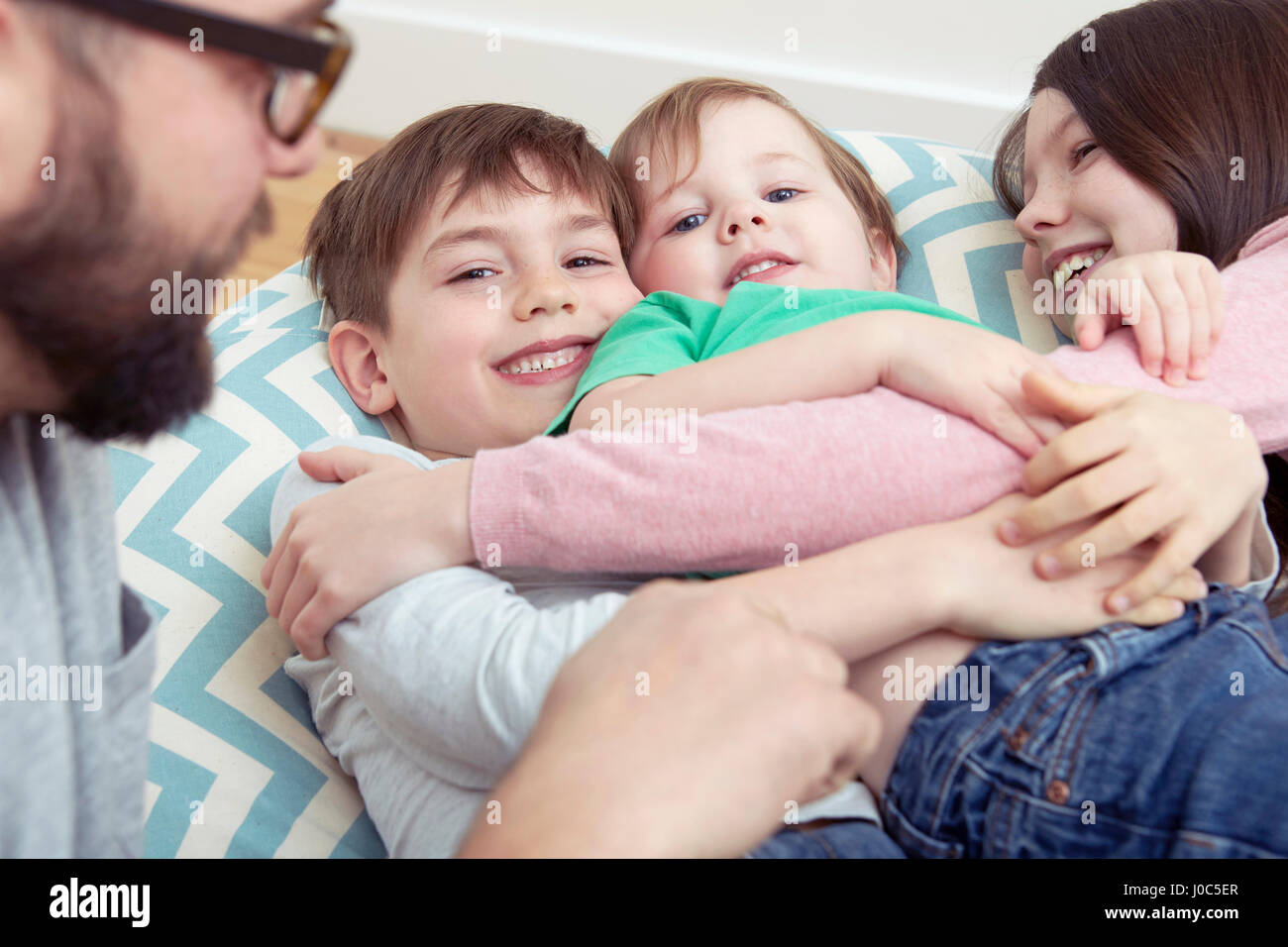 Padre e tre bambini sorridenti reclinata su sedia beanbag Foto Stock