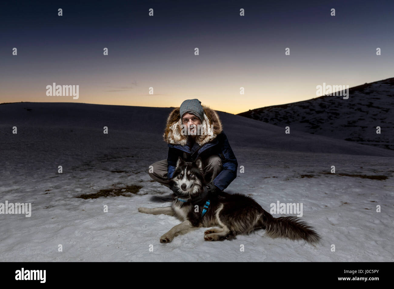 Ritratto di uomo maturo accovacciato con il cane nella neve durante la notte Foto Stock