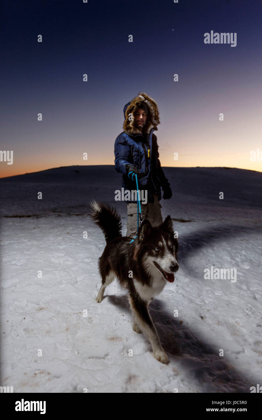 Uomo maturo cane a camminare nella neve durante la notte Foto Stock