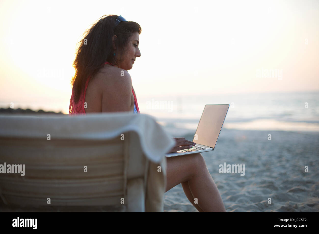 Donna matura seduto sulla spiaggia sdraio guardando laptop, Dubai, Emirati Arabi Uniti Foto Stock