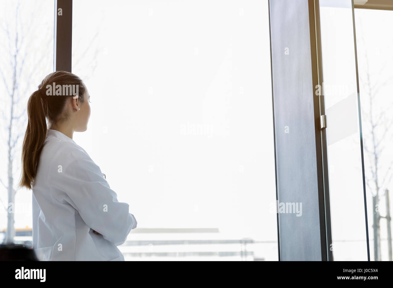 Medico donna guardando fuori della finestra, vista posteriore Foto Stock