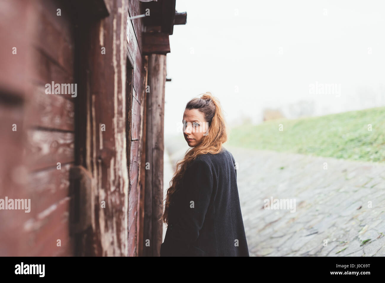 Ritratto di giovane donna guardando sopra la sua spalla dalla capanna spiovente Foto Stock