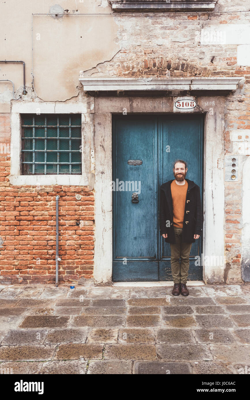 Ritratto di barbuto metà uomo adulto in piedi nella parte anteriore della vecchia porta, Venezia, Italia Foto Stock