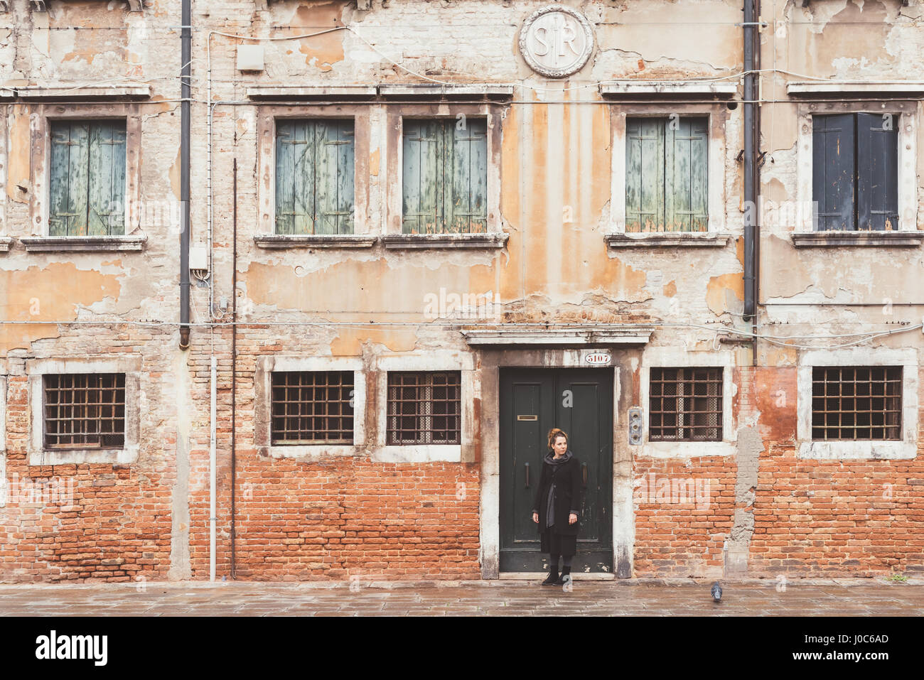 Giovane donna guardando sopra la sua spalla dalla vecchia porta, Venezia, Italia Foto Stock