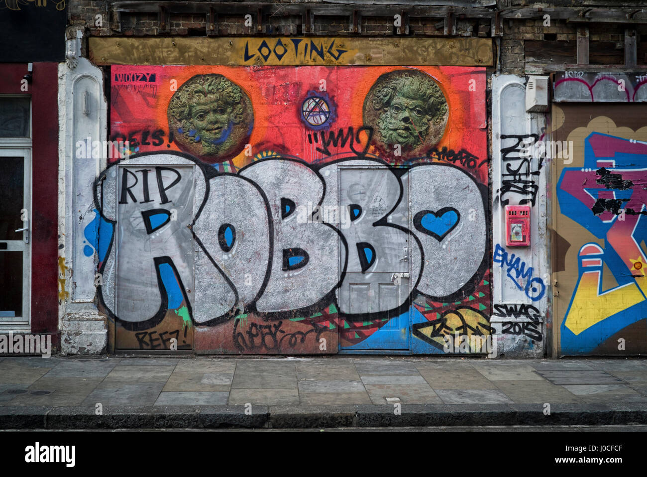 Robbo RIP graffiti in memoria del passaggio di artista di strada Robbo dipinta su shop serrande della Bethnal Green Road, Londra, vicino a Brick Lane Foto Stock