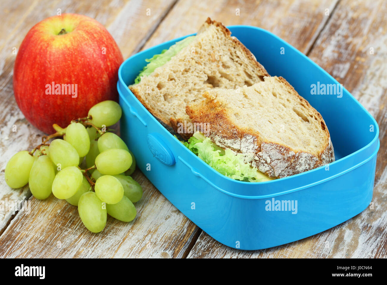 Scuola pranzo composto da pane rustico panini con formaggio e lattuga, apple e uva Foto Stock