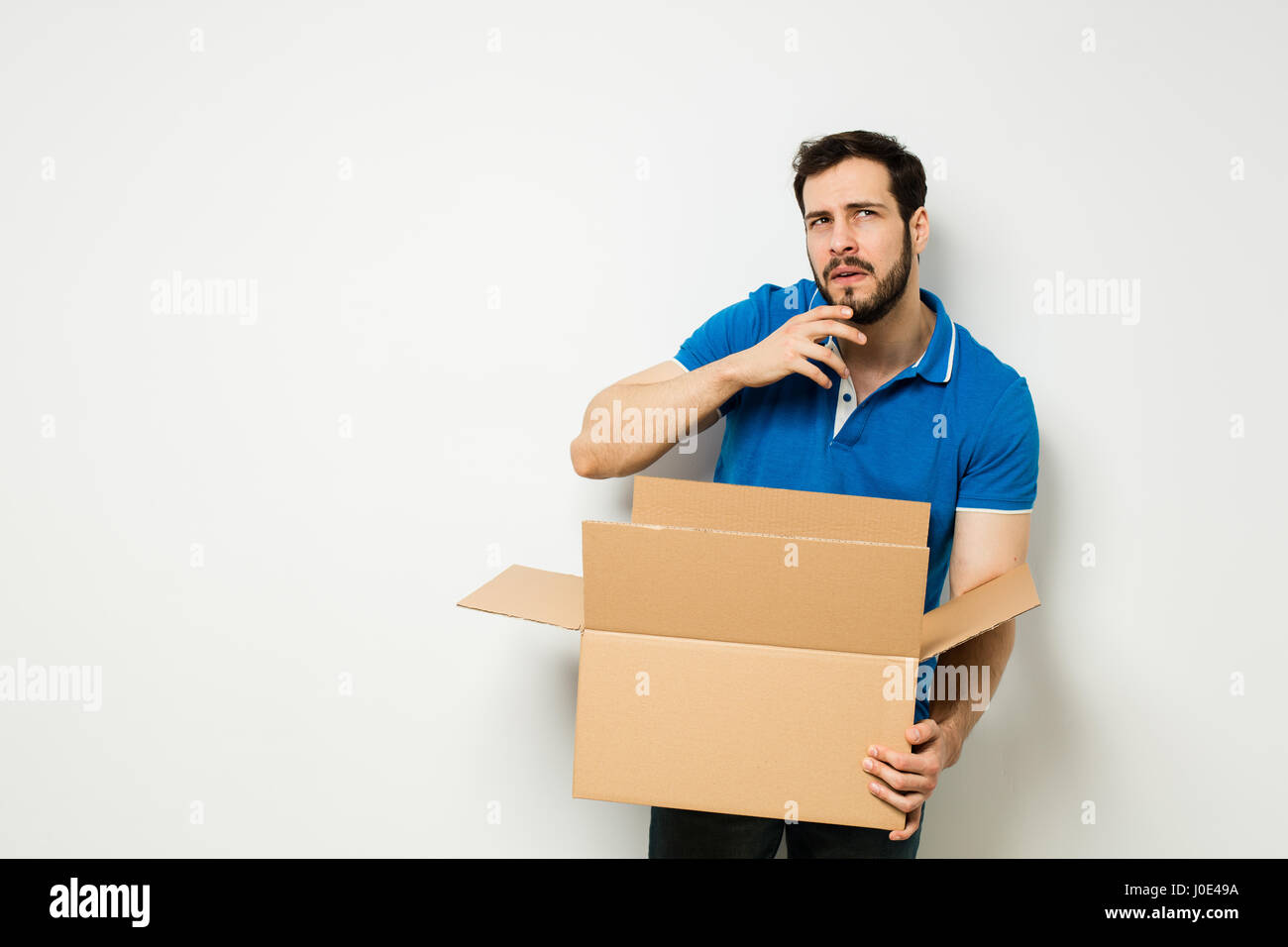 Confuso uomo cerchi qualcosa in una scatola di cartone su una parete bianca Foto Stock