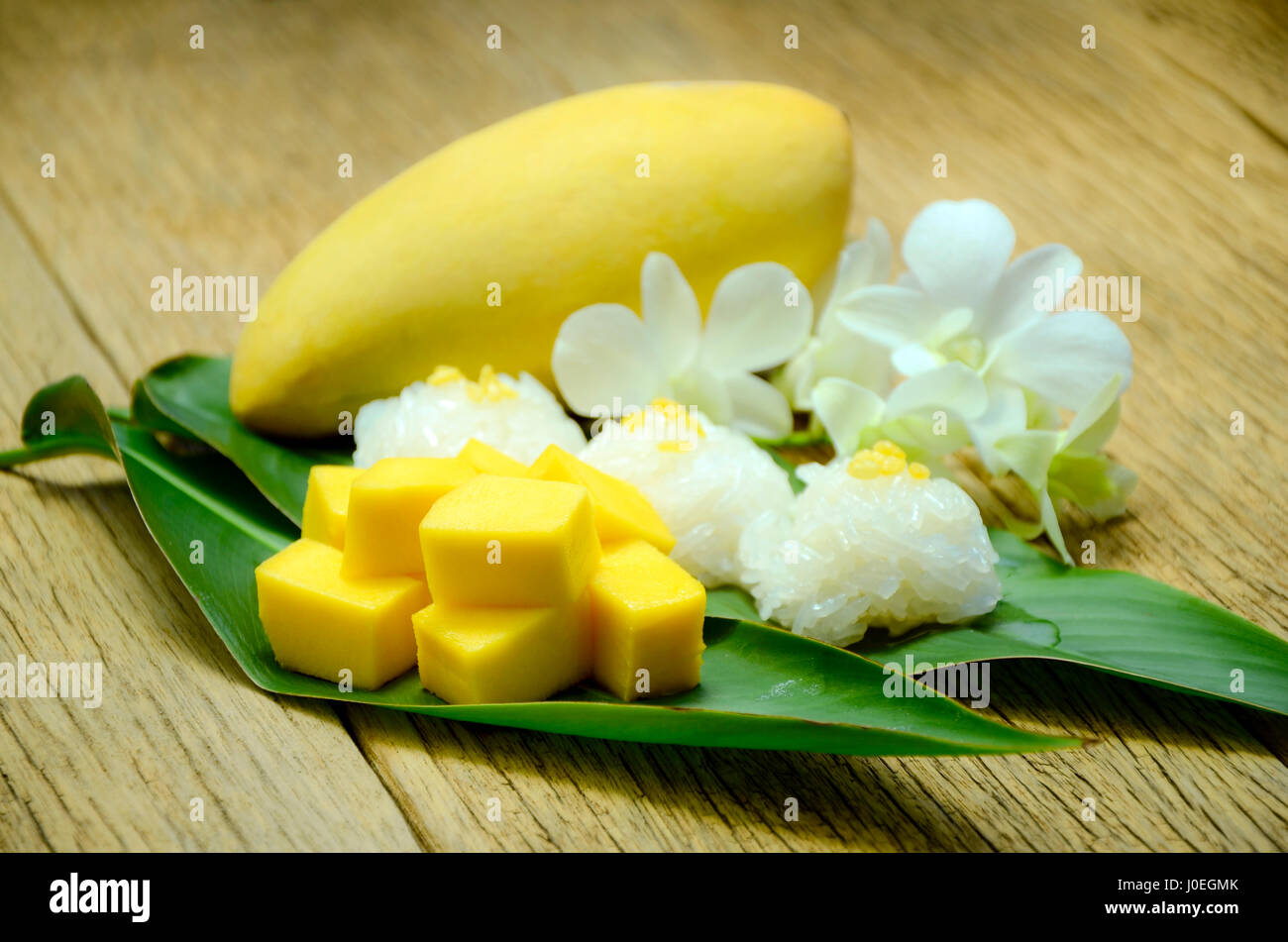 Thai dessert. Sweet mango con i dolci di riso e latte di cocco per topping servita su fresche foglie verdi con decor di bianco del tailandese Orchidee. Foto Stock