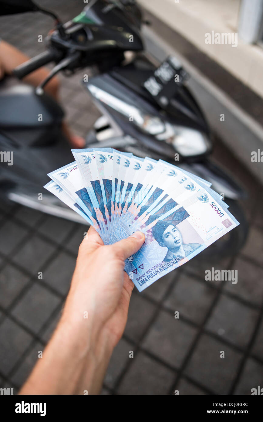 Noleggia o acquista una moto o uno scooter in Indonesia. Sacco di contanti (Rupiah indonesiano) in mano. Deposito truffa o di pagare per un crash bike. Isola di Bali. Foto Stock