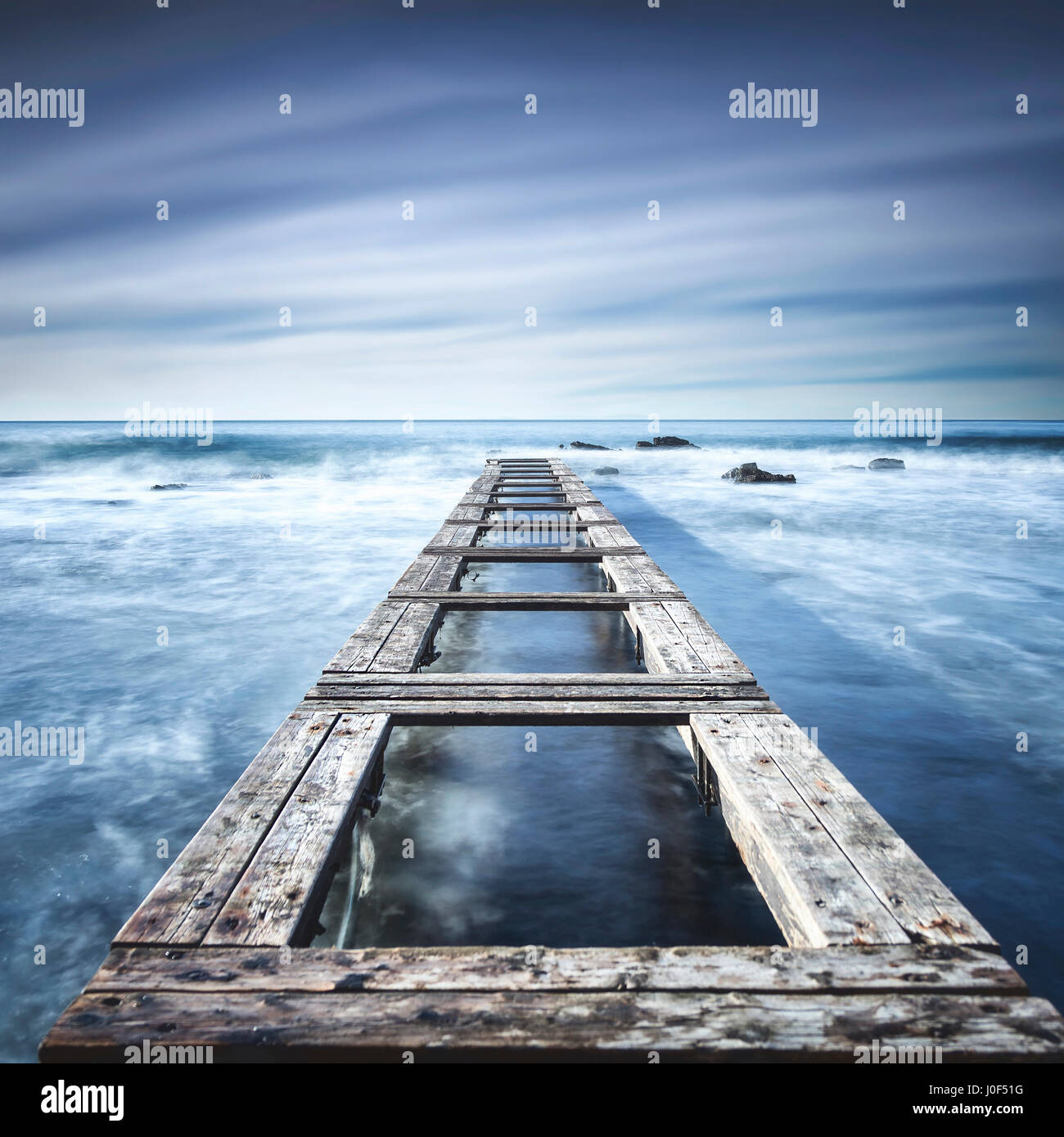 Il molo di legno o un pontile e scogli su un oceano blu. Esposizione lunga Foto Stock