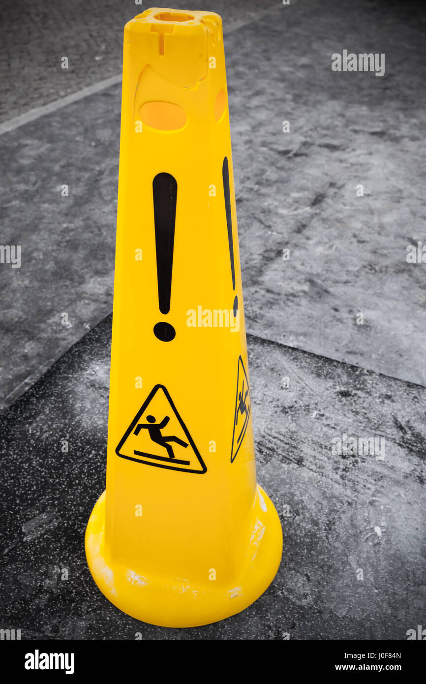 Attenzione pavimento bagnato, simbolo giallo di avvertimento si erge su grigio asfalto Terreno urbano Foto Stock