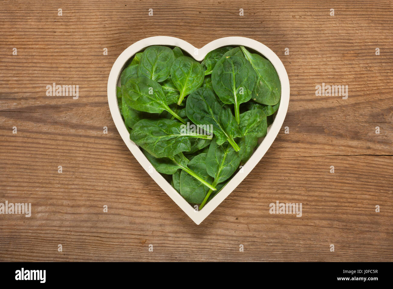 Spinaci freschi di foglie in un recipiente a forma di cuore Foto Stock
