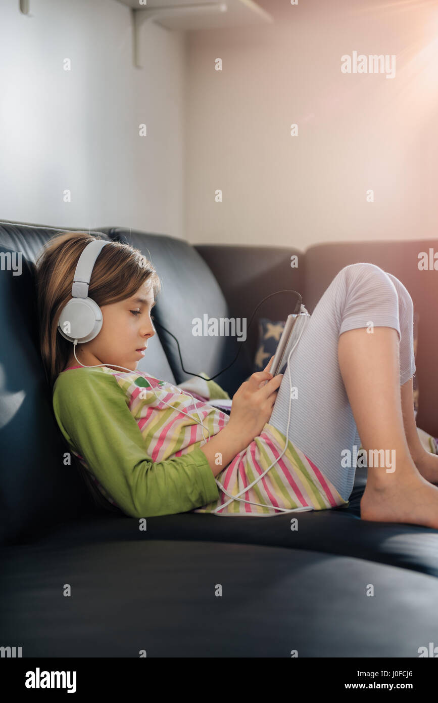 Ragazza seduta sul divano nero utilizzando tablet e ascolto di musica Foto Stock