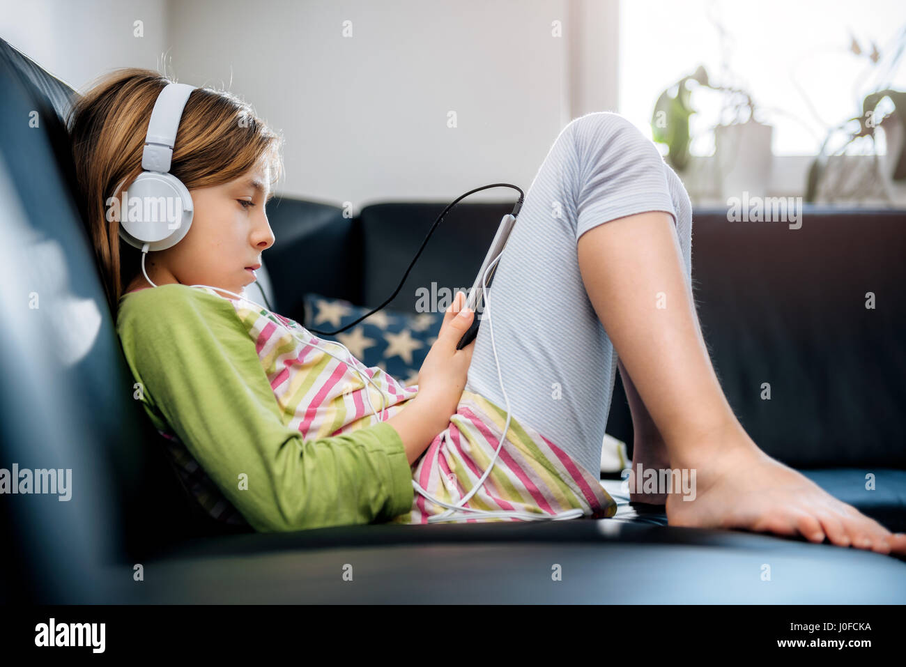 Ragazza seduta sul divano nero utilizzando tablet e ascolto di musica Foto Stock