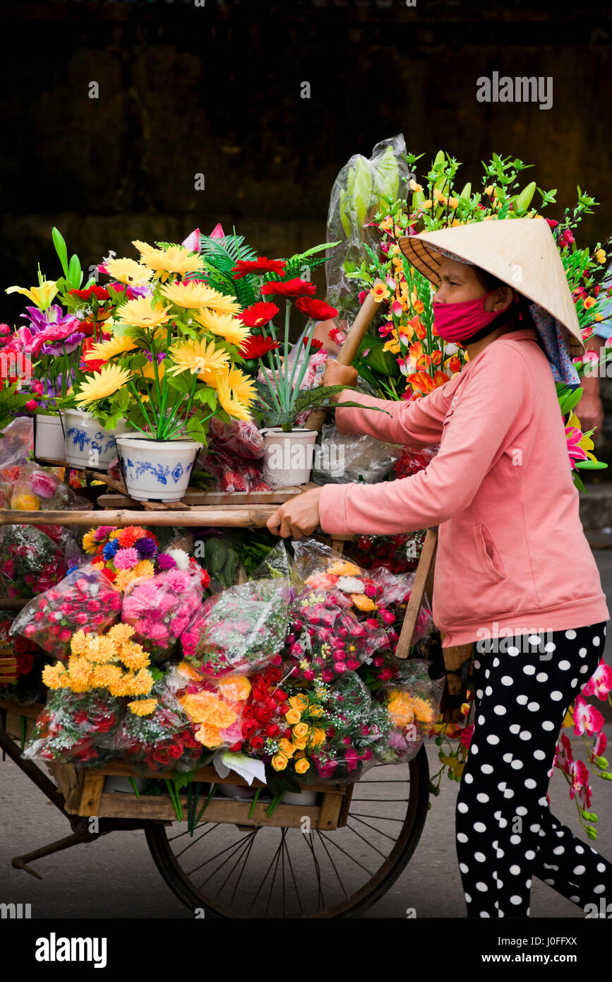 Ritratto verticale di una signora che vendono fiori dalla parte posteriore di una bicicletta in Hoi An, Vietnam. Foto Stock