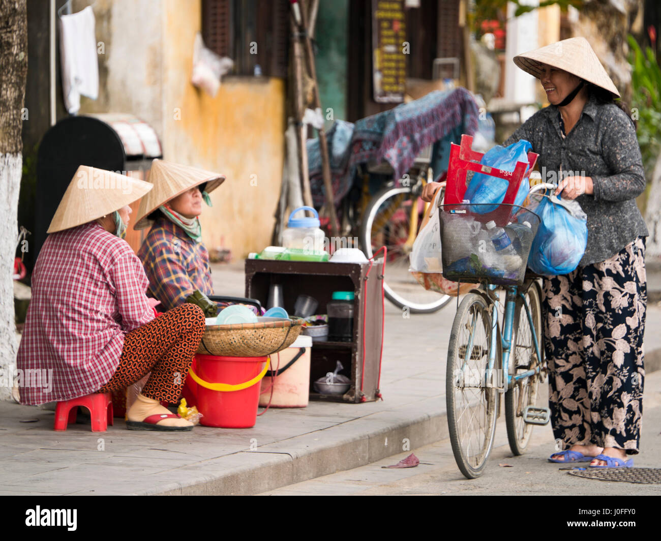 Vista orizzontale di ladies in tradizionali cappelli conici aventi un gossip sulle strade in Hoi An, Vietnam. Foto Stock