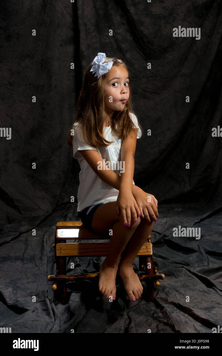 Bambina la modellazione in studio sfondo marrone ubicazione su una sedia di legno Foto Stock