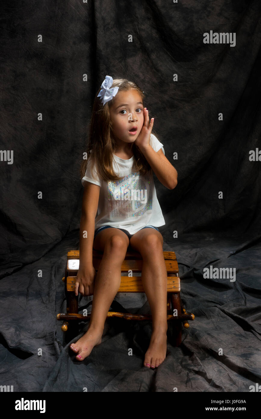 Bambina la modellazione in studio sfondo marrone ubicazione su una sedia di legno Foto Stock