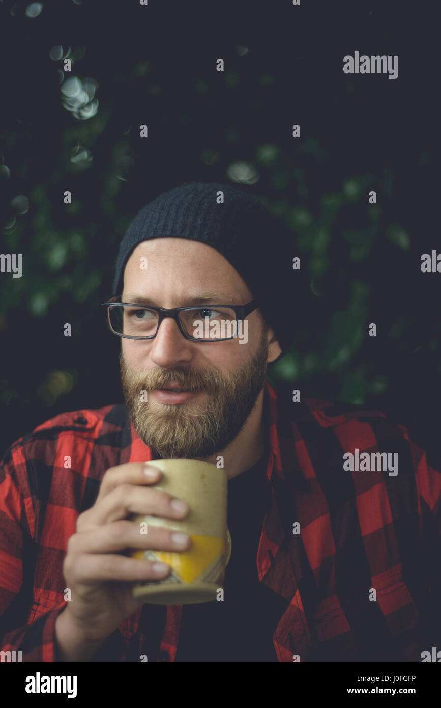 Un autentico ritratto di una bella e felice hipster uomo seduto sulla veranda a bere caffè. Foto Stock