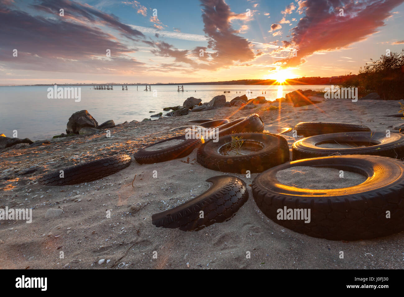 Un sacco di pneumatici sprecato sulla spiaggia al tramonto Foto Stock
