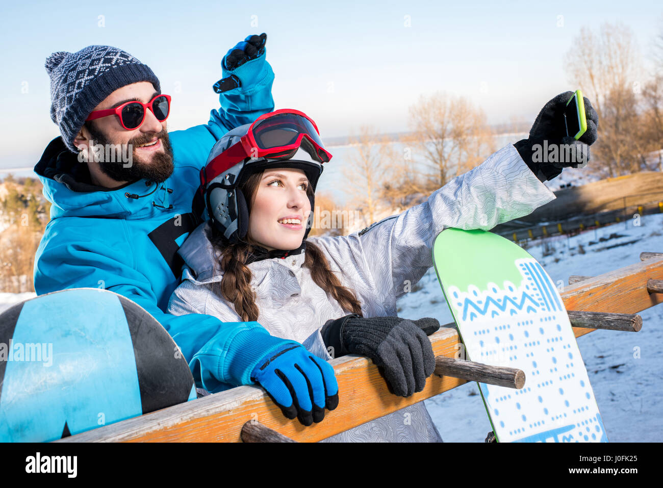 Giovane uomo e donna abbracciando e tenendo selfie con racchette da neve Foto Stock