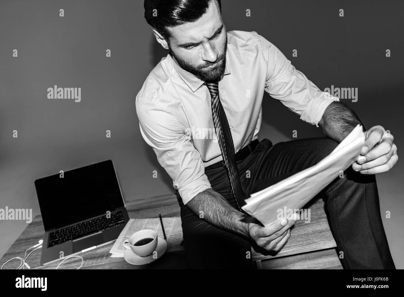 Ritratto in bianco e nero di imprenditore seduto sul tavolo e la lettura dei documenti Foto Stock