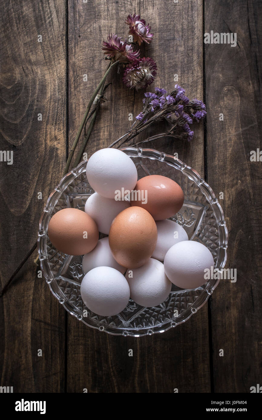 Marrone e bianco uova di pollo nella ciotola di vetro sul tavolo di legno Foto Stock