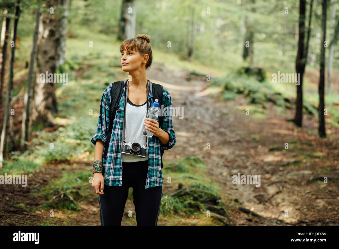 Traveler donna in mezzo alla foresta a piedi con il suo zaino e una bottiglia di acqua minerale, scoprendo la natura intorno a lei Foto Stock