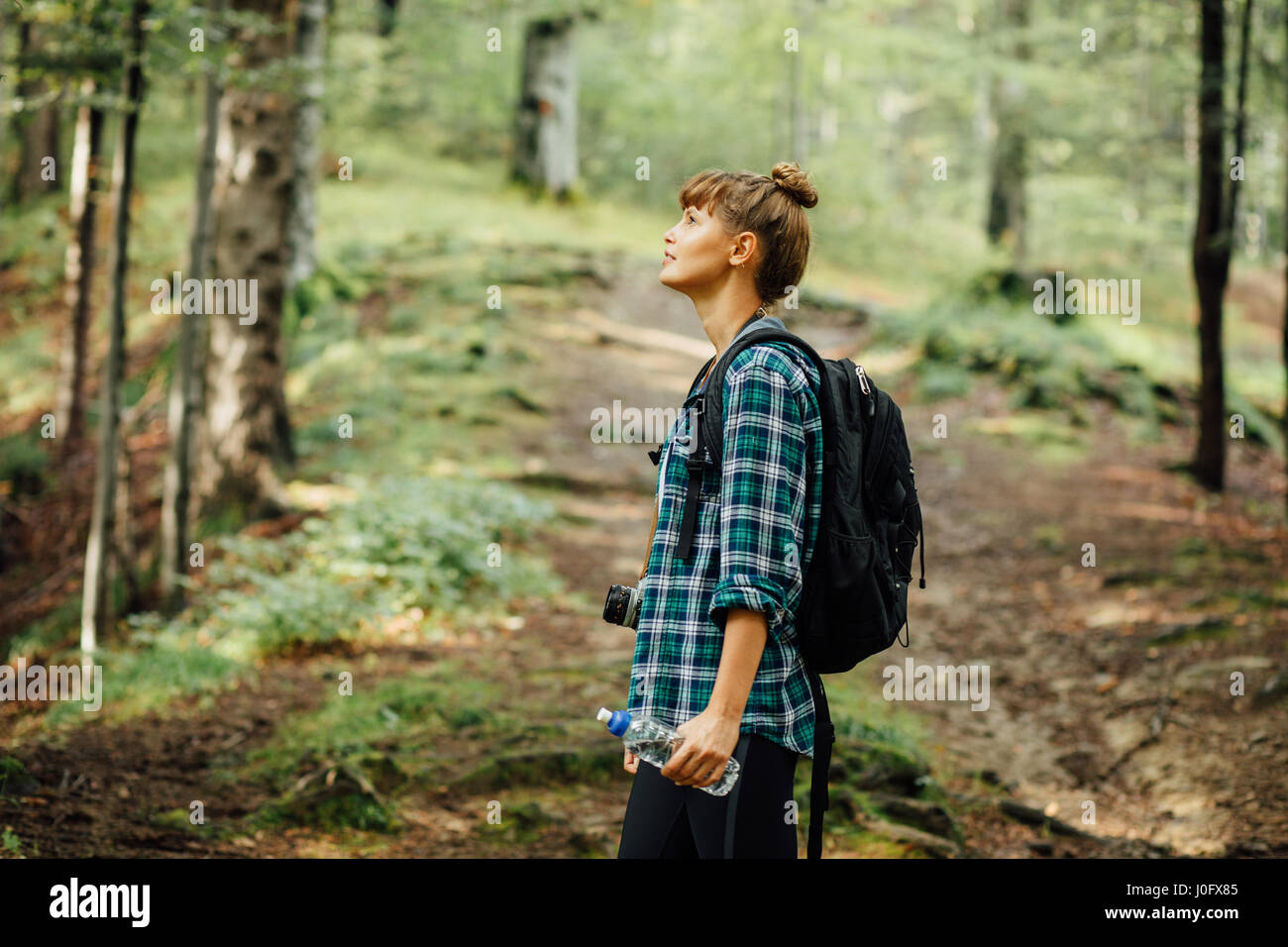 Traveler donna in mezzo alla foresta a piedi con il suo zaino e una bottiglia di acqua minerale, scoprendo la natura intorno a lei Foto Stock