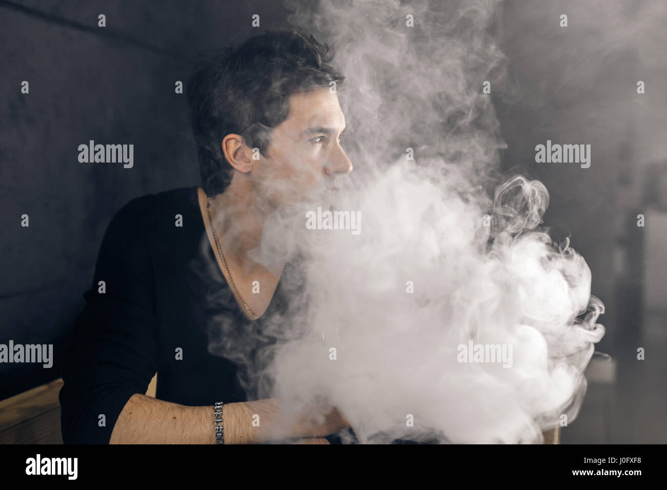 Uomo Vaping tenendo un mod. Una nuvola di vapore. Sfondo nero. Foto Stock