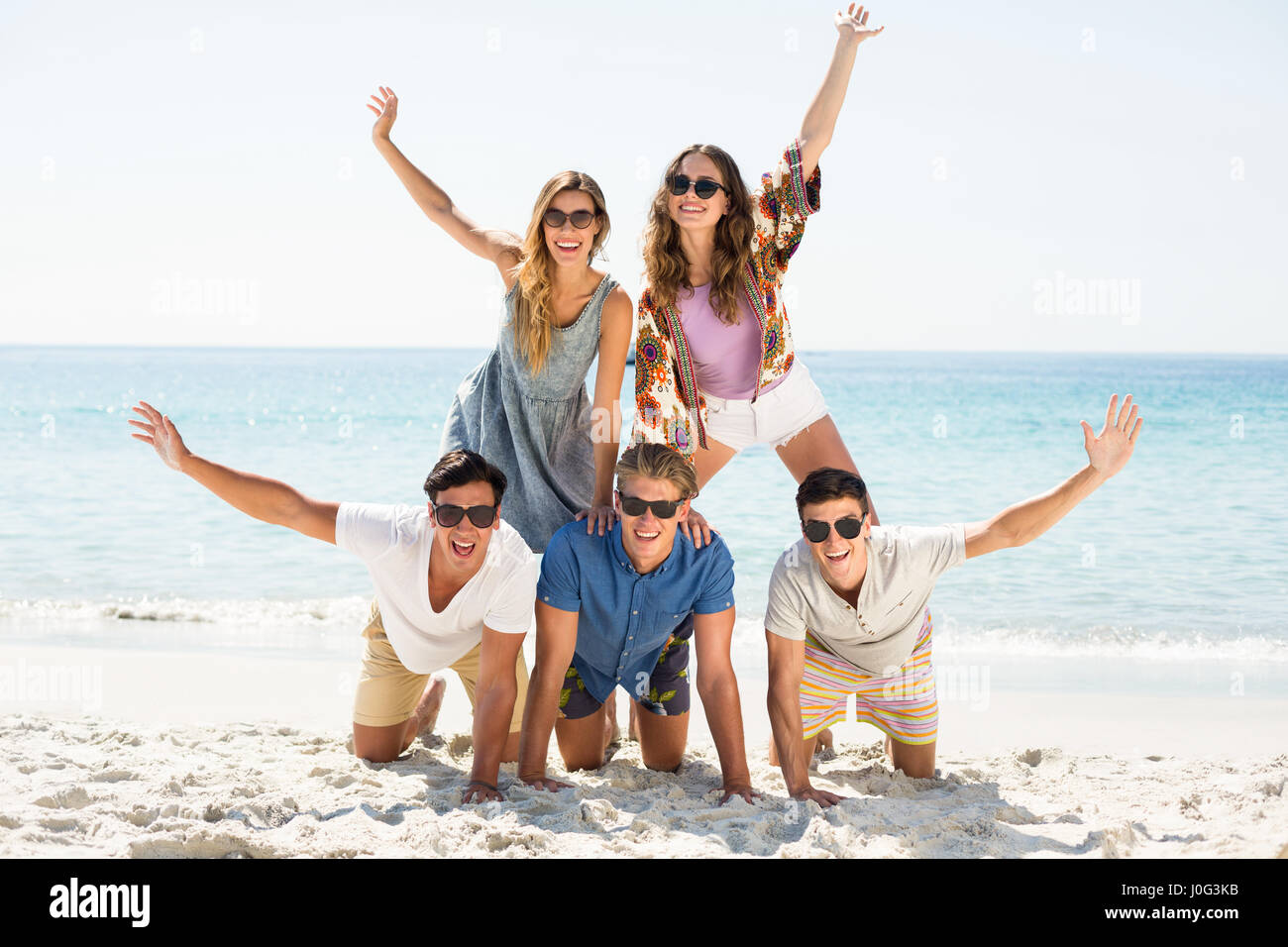 Allegro amici piramide di formatura con le braccia sollevate in spiaggia sulla giornata di sole Foto Stock