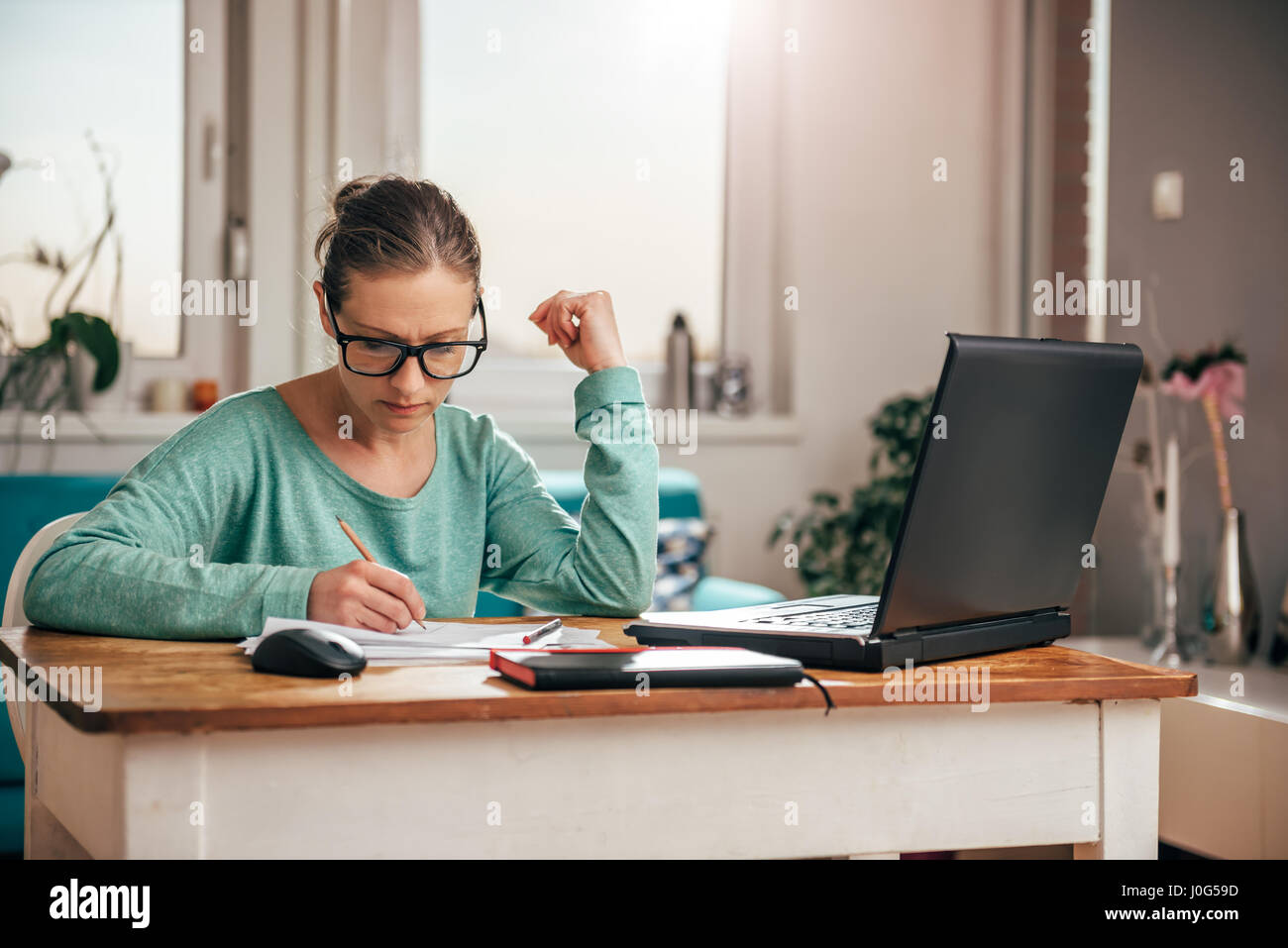 Donna che indossa occhiali seduti ad una scrivania a casa e di fare la documentazione Foto Stock