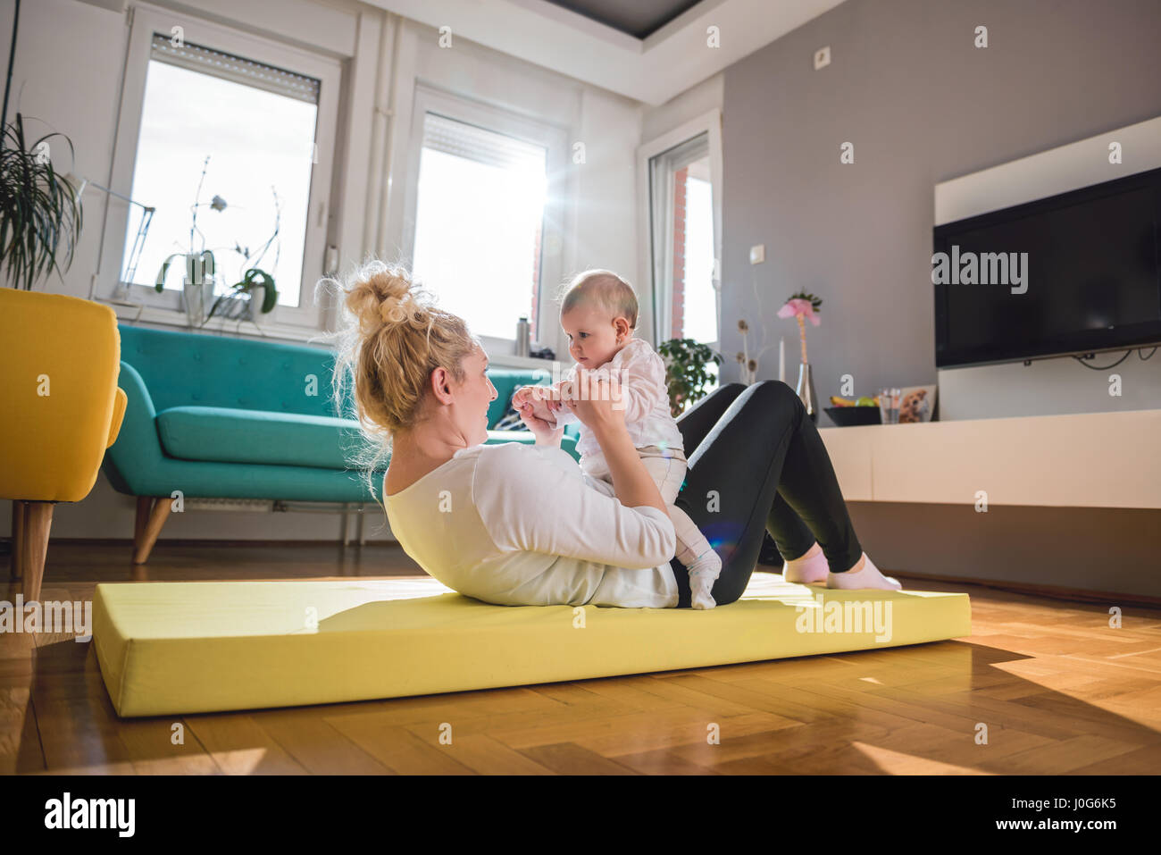 Esercizio di madre con il suo bambino sul tappeto giallo a casa Foto Stock