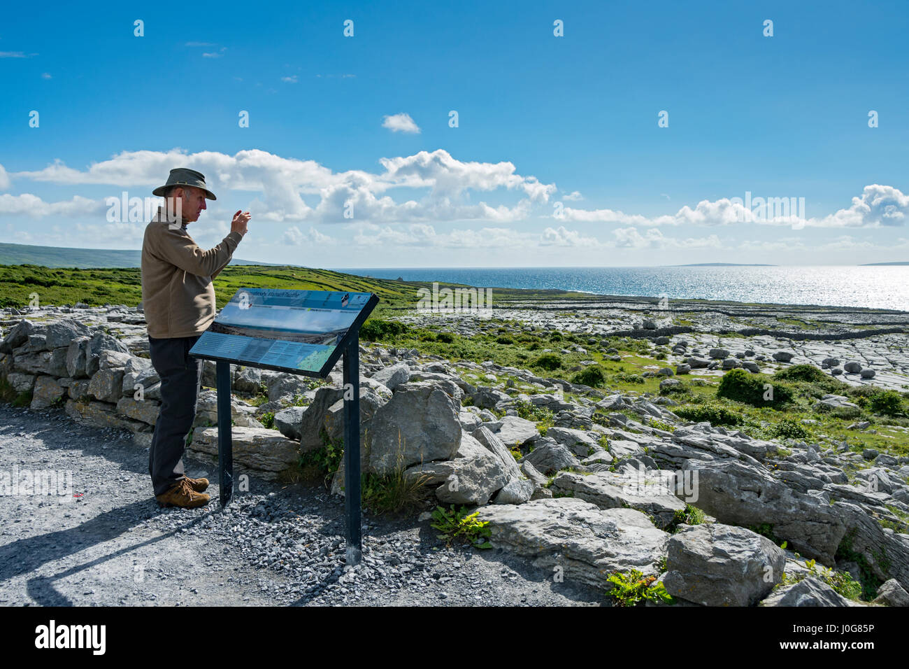 Un turista a fotografare il calcare pavimentazione mediante una scheda di informazioni a Murrooghtoohy, Burren, County Clare, Irlanda Foto Stock