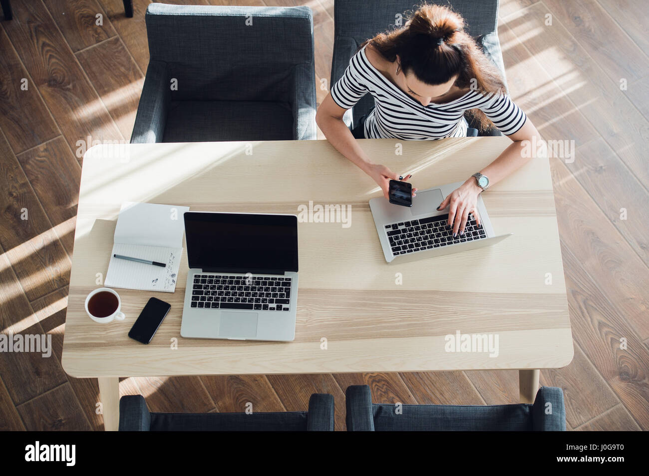 Vista superiore della femmina usando il suo computer portatile a un cafe'. Tettuccio di colpo di giovane donna seduta al tavolo con una tazza di caffè e telefono cellulare navigando in rete sul suo computer portatile. Foto Stock