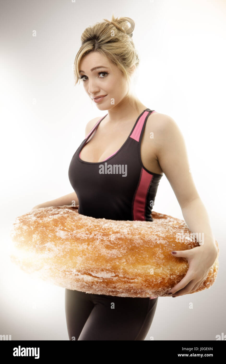 Donna fitness con una ciambella di grandi dimensioni attorno alla sua vita simboleggiano la messa sul peso Foto Stock