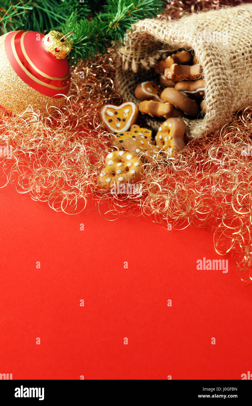 Decorazione di natale come il ramoscello di pino, ornamento di Natale e sacco di iuta con prezel e cookie sul rosso spazio di copia Foto Stock