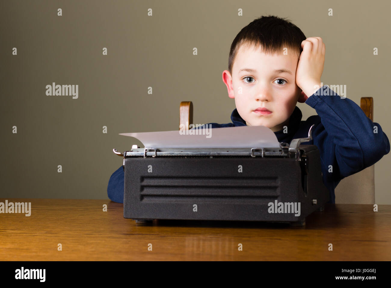Carino piccolo ragazzo cerca distratti nella parte anteriore di un nero vintage macchina da scrivere a casa Foto Stock
