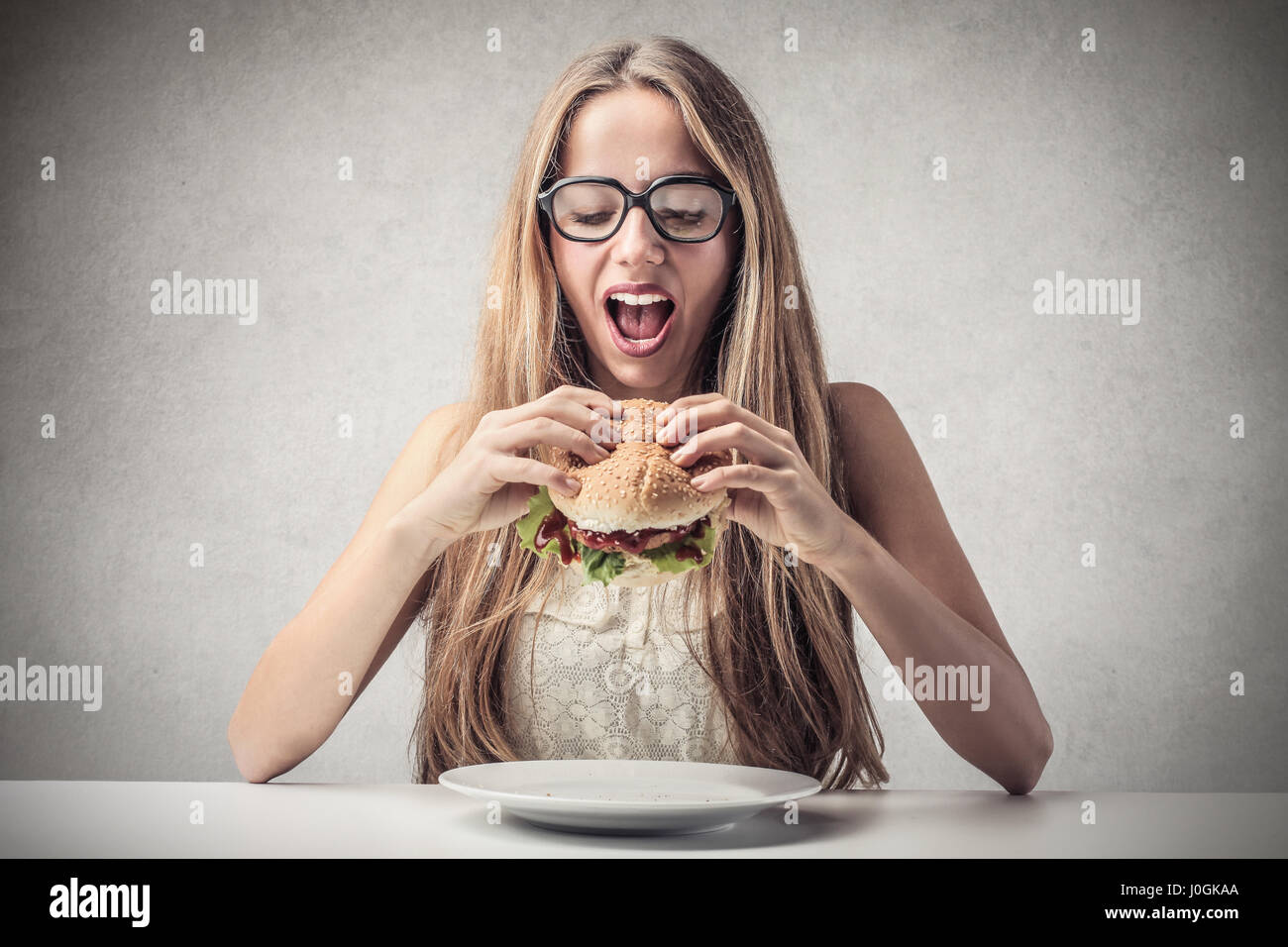 Donna bionda mangiare hamburger Foto Stock