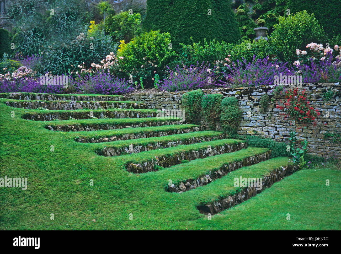 Fasi di erba con una bordatura di fiori che crescono lungo la terrazza nel south lawn a Misarden Park Foto Stock