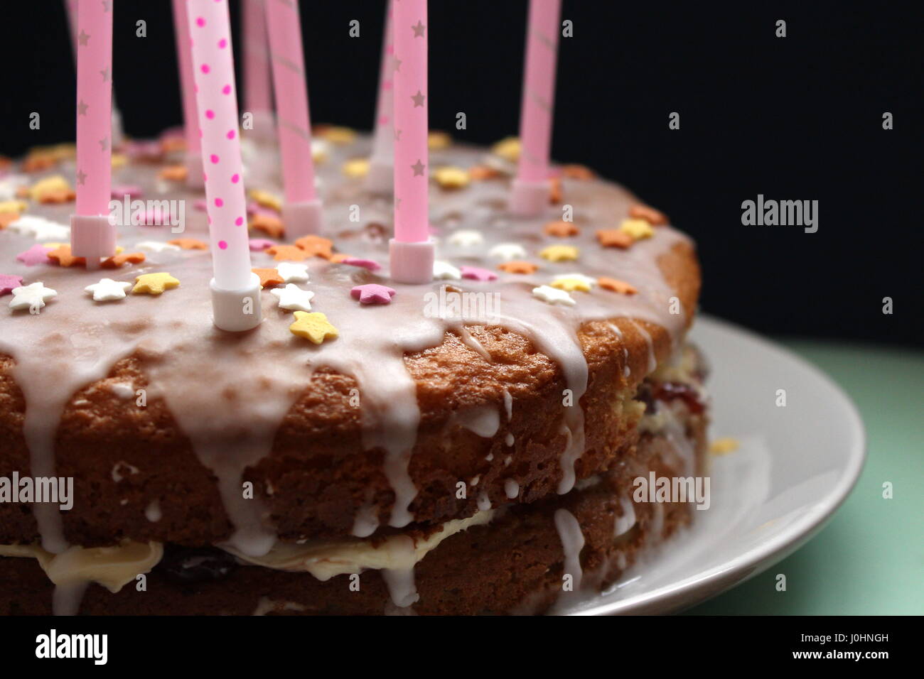 Compleanno victoria sponge cake con glassa che cola e rosa candele, con zucchero star decorazioni, contro uno sfondo nero Foto Stock