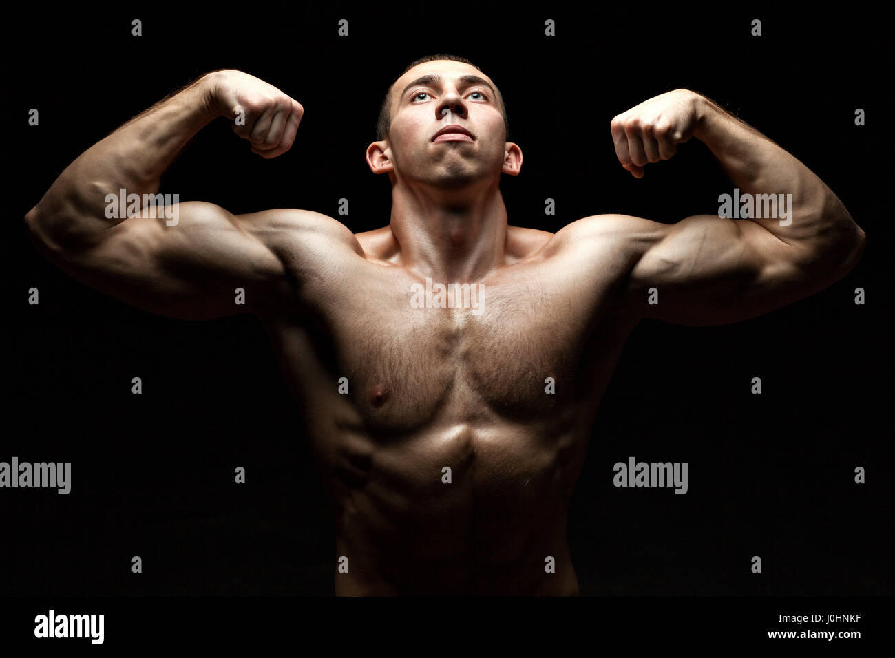 Ritratto di un culturista che costruire il muscolo e ci mostra allo stesso tempo cercando su sfondo nero. Foto Stock