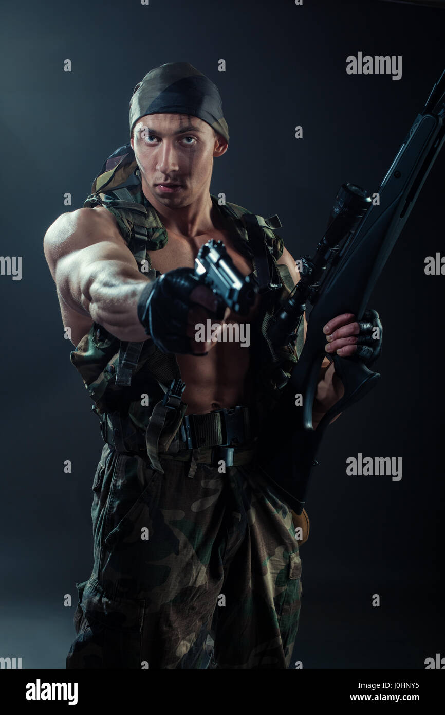 Un uomo con un enorme di muscoli, è in forma di hacks nelle mani in possesso di una pistola e un fucile. Foto Stock