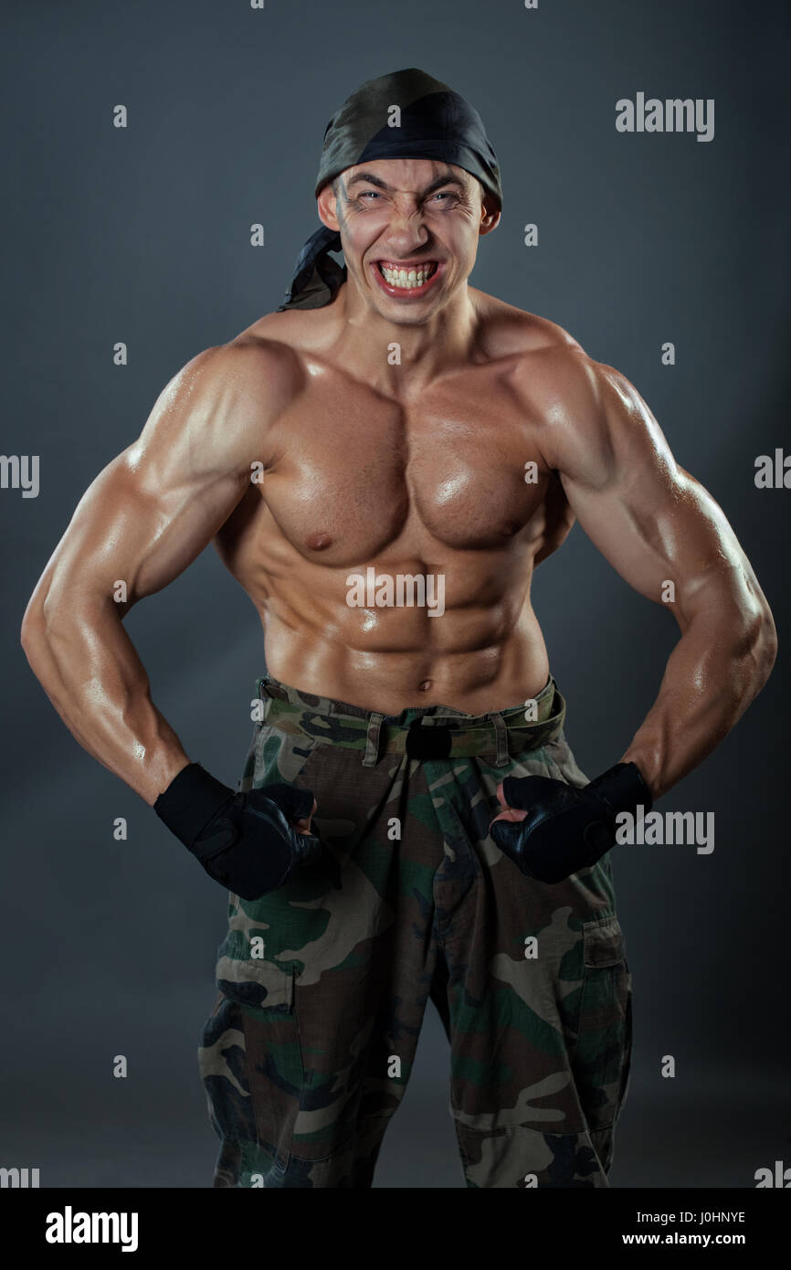 Un uomo in pantaloni militari mostra il suo enorme muscoli. Esso è fortemente muscoli tesi e faccia grimace ritorto. Foto Stock